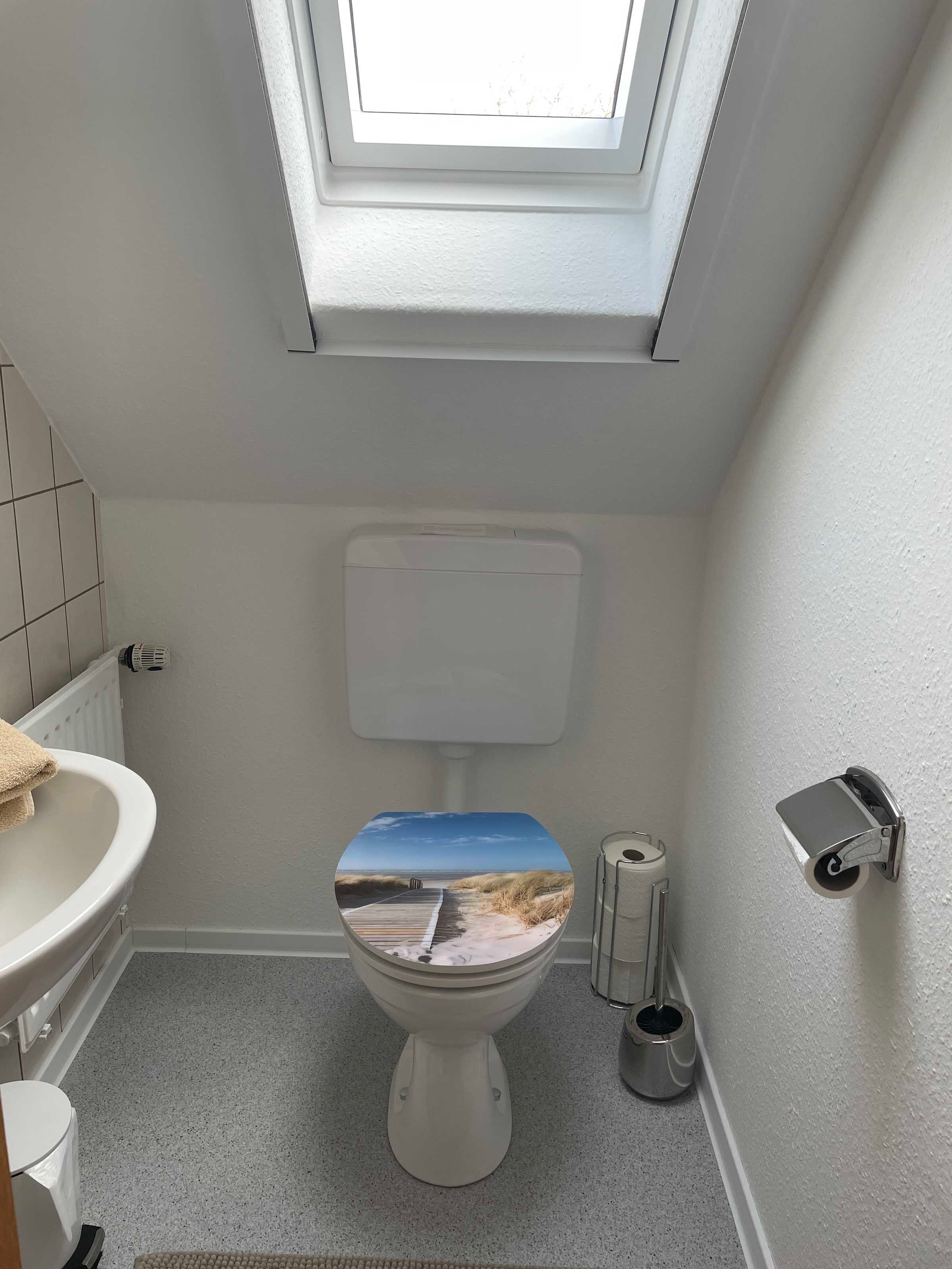 Ein Badezimmer mit Dachfenster, einer Toilette mit Strandmotiv, einem Waschbecken und einem Bidet.
