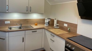 A modern kitchen with white cabinets, a wooden countertop, a sink, a coffee maker, and a black range hood. - Haus Landruhe, Deutschland (Neuharlingersiel)