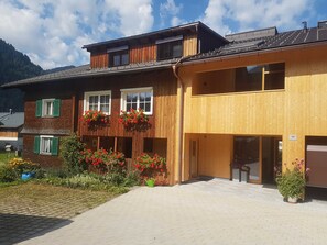 A two-story building with a wooden facade, large windows, and flower boxes on the second floor. - 2-room vacation apartment - Felder Apartments (Schoppernau)