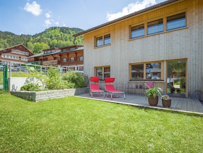 A modern wooden building with a deck, red lounge chairs, and a garden area.