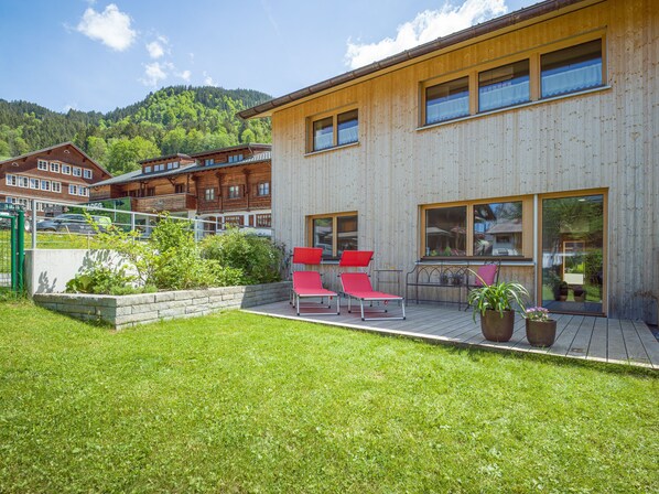 A modern wooden building with a deck, red lounge chairs, and a garden area. - 2-room vacation apartment - Felder Apartments (Schoppernau)