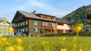 A two-story wooden house with a sloped roof, large windows, and a balcony. - Vacation apartment 2 rooms - Felder Apartments (Schoppernau)