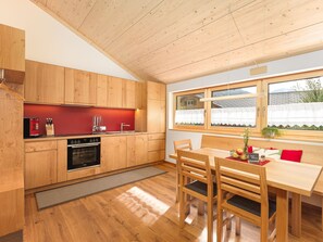A modern kitchen with wooden cabinets, a red countertop, and a dining area with a wooden table and chairs. - 2-room vacation apartment - Felder Apartments (Schoppernau)