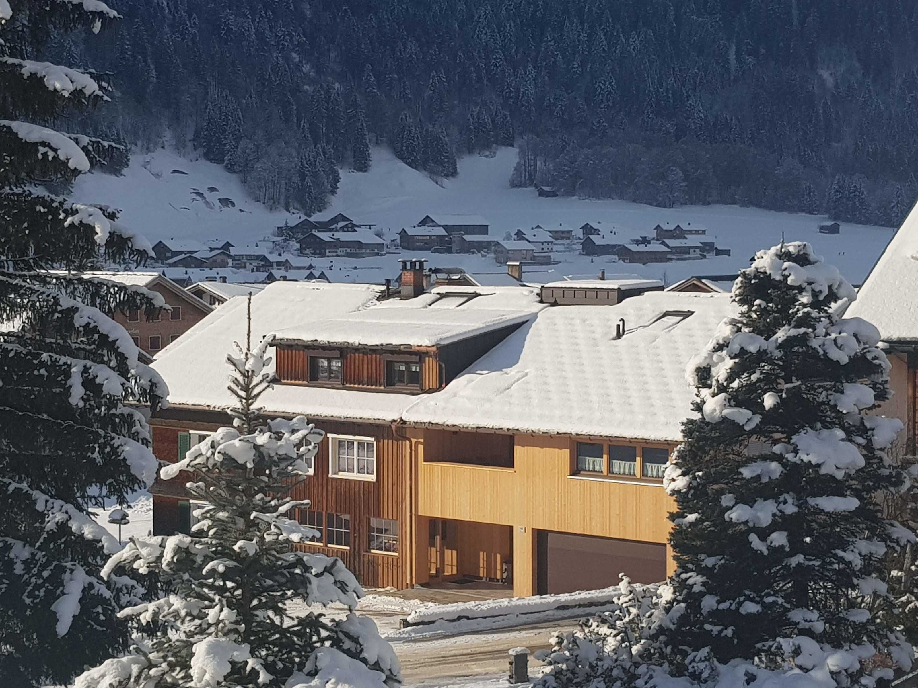 Ein Holzbau mit Garage, umgeben von schneebedeckten Bäumen und einer Bergkulisse.