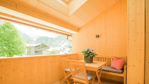 Un balcone in legno con tavolo e sedie, una pianta in vaso e vista su edifici e alberi.