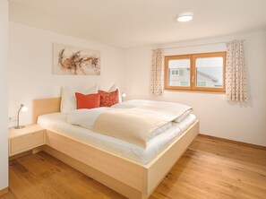 Ein Schlafzimmer mit Bett, Nachttisch, Lampe, einem Fenster mit Vorhängen und einem Bild an der Wand.
