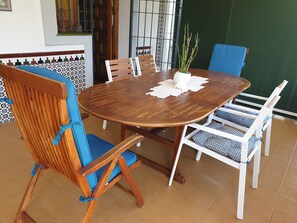 Taula rodona de fusta amb un vas blanc i una planta, envoltada de cadires blanques amb coixins blaus.
