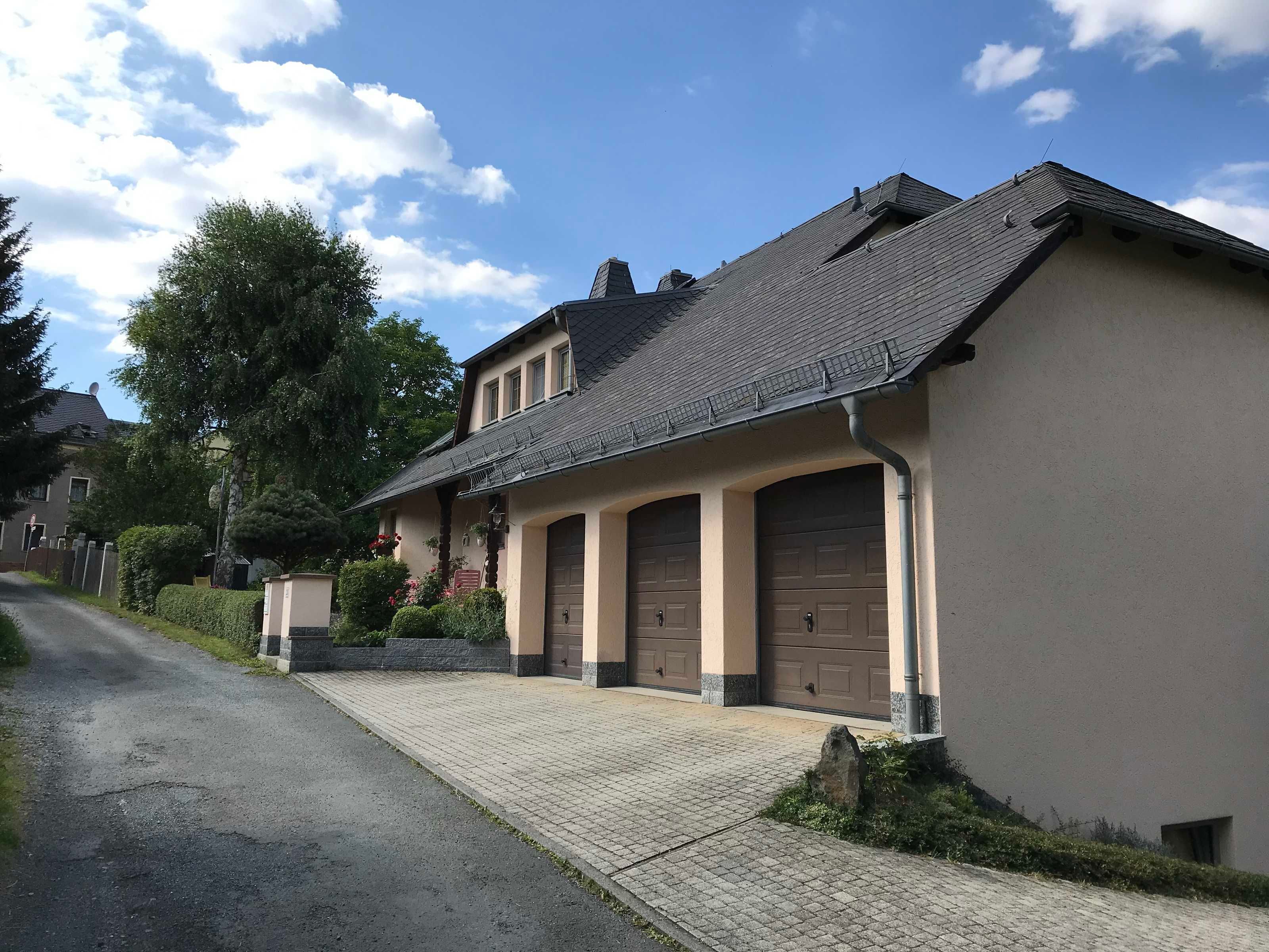 A two-story house with a tiled roof, two garage doors, and a paved driveway.
