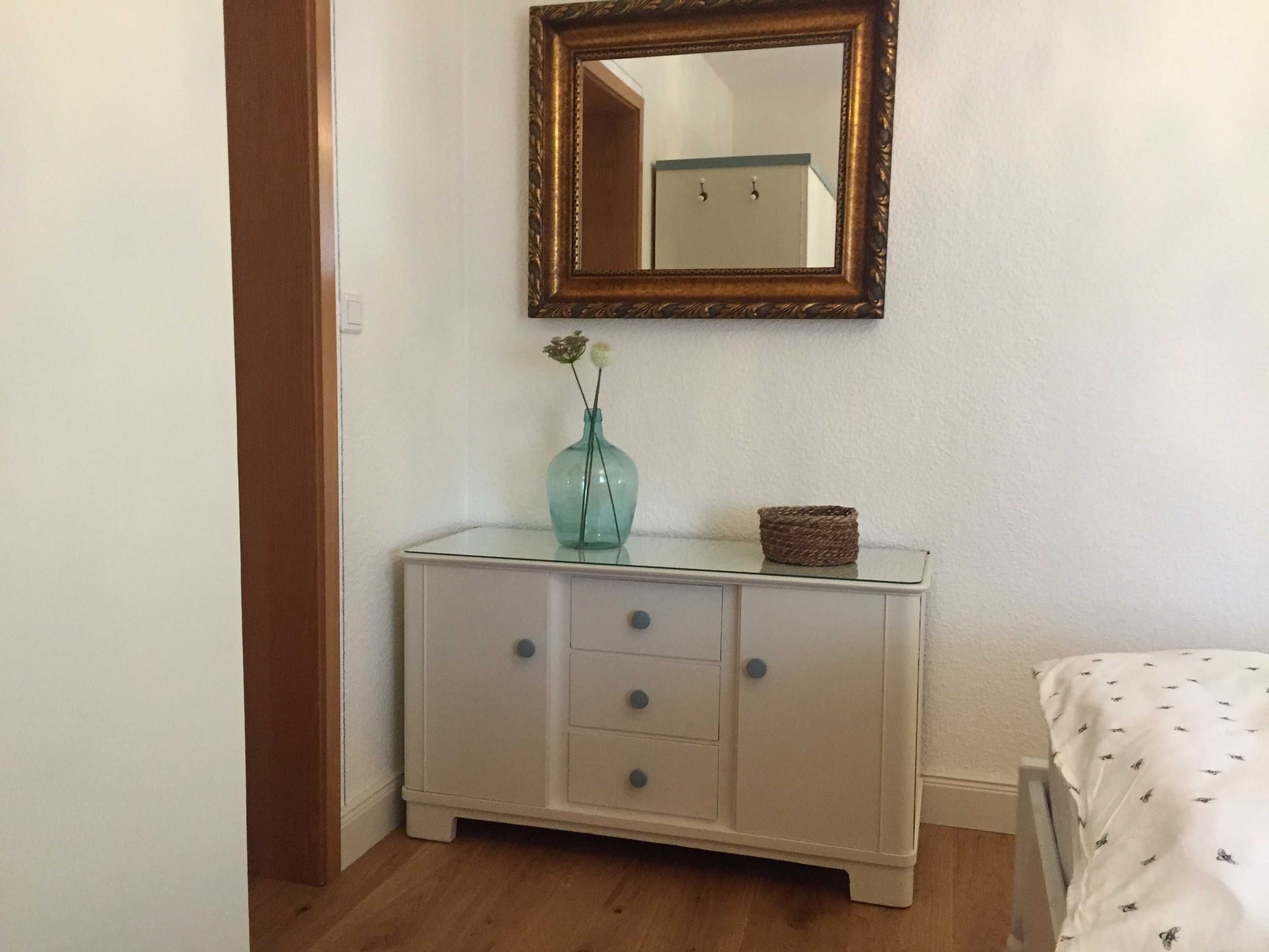 Ein Zimmer mit einem weißen Schrank, einem Spiegel und einer Vase mit Blumen.