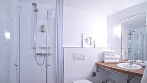 Un baño moderno con cabina de ducha de vidrio, inodoro blanco, lavamanos con encimera de madera y espejo.