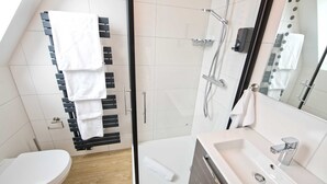 Une salle de bain moderne avec une douche à parois de verre, un lavabo blanc et un porte-serviettes avec plusieurs serviettes.