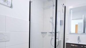 Ein modernes Badezimmer mit einer Glaskabine zur Dusche, einer weißen Toilette und einem dunklen Holzwaschtisch.