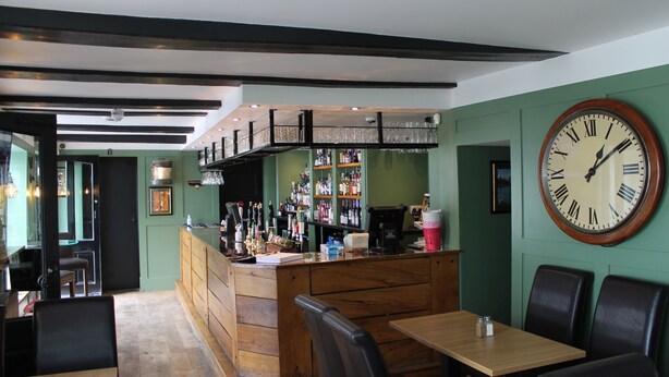 Un restaurante con zona de bar, mobiliario de madera y un gran reloj de pared.