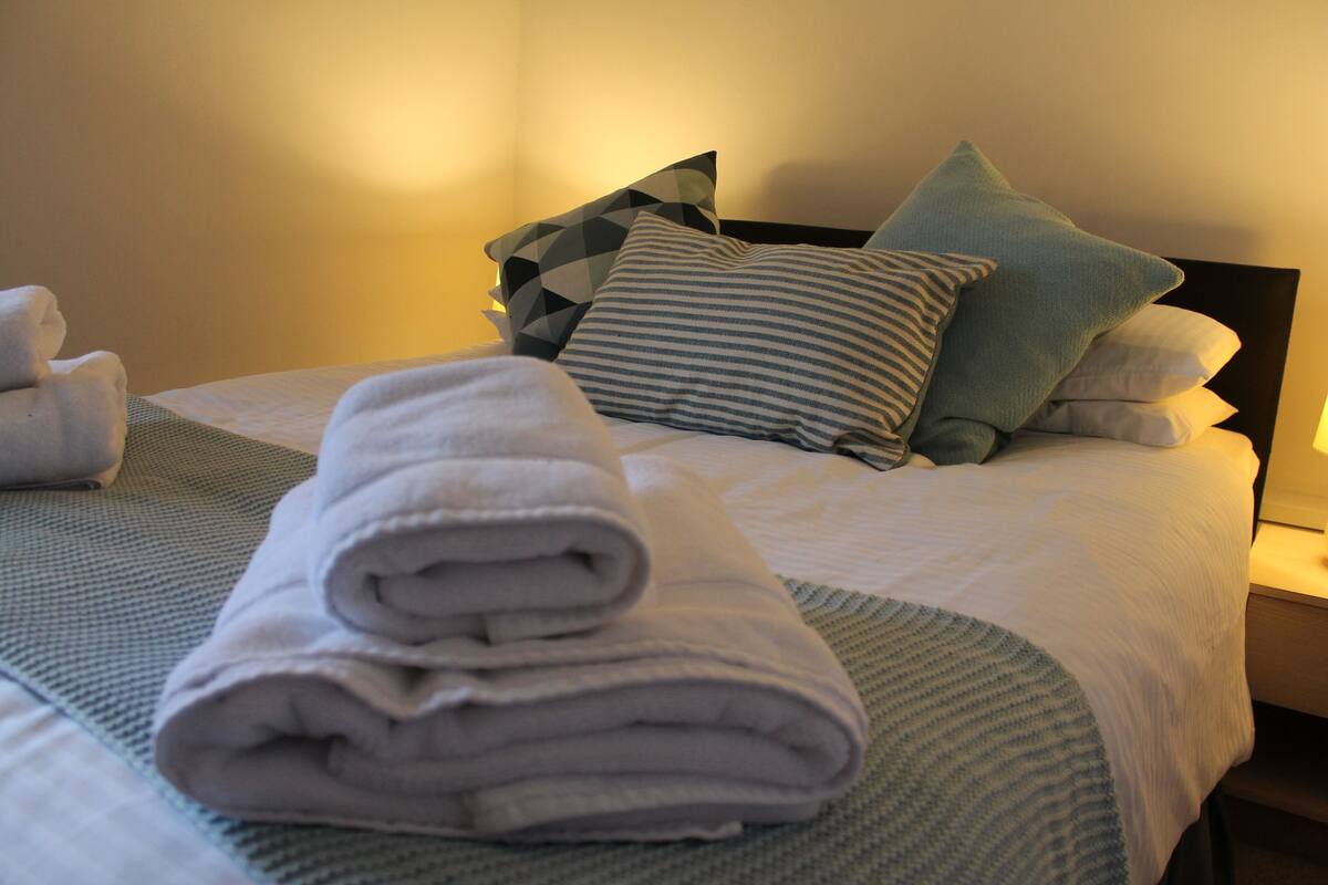 A neatly made bed with a folded towel, pillows, and a blanket.
