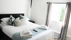 Una cama bien hecha con almohadas, un control remoto y toallas dobladas.
