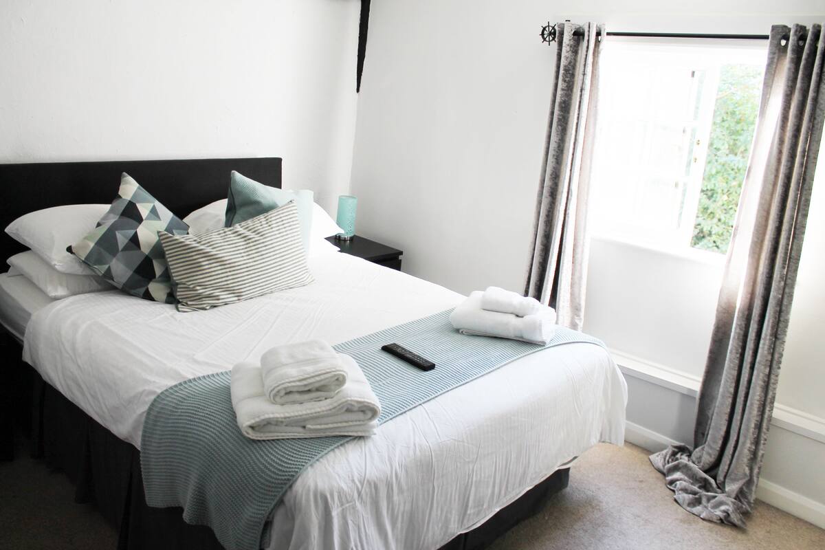 A neatly made bed with pillows, a remote control, and folded towels.