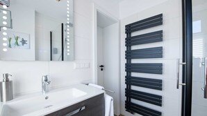 A modern bathroom with a white sink, a mirror with lights, a towel rack, and a door with a black handle.