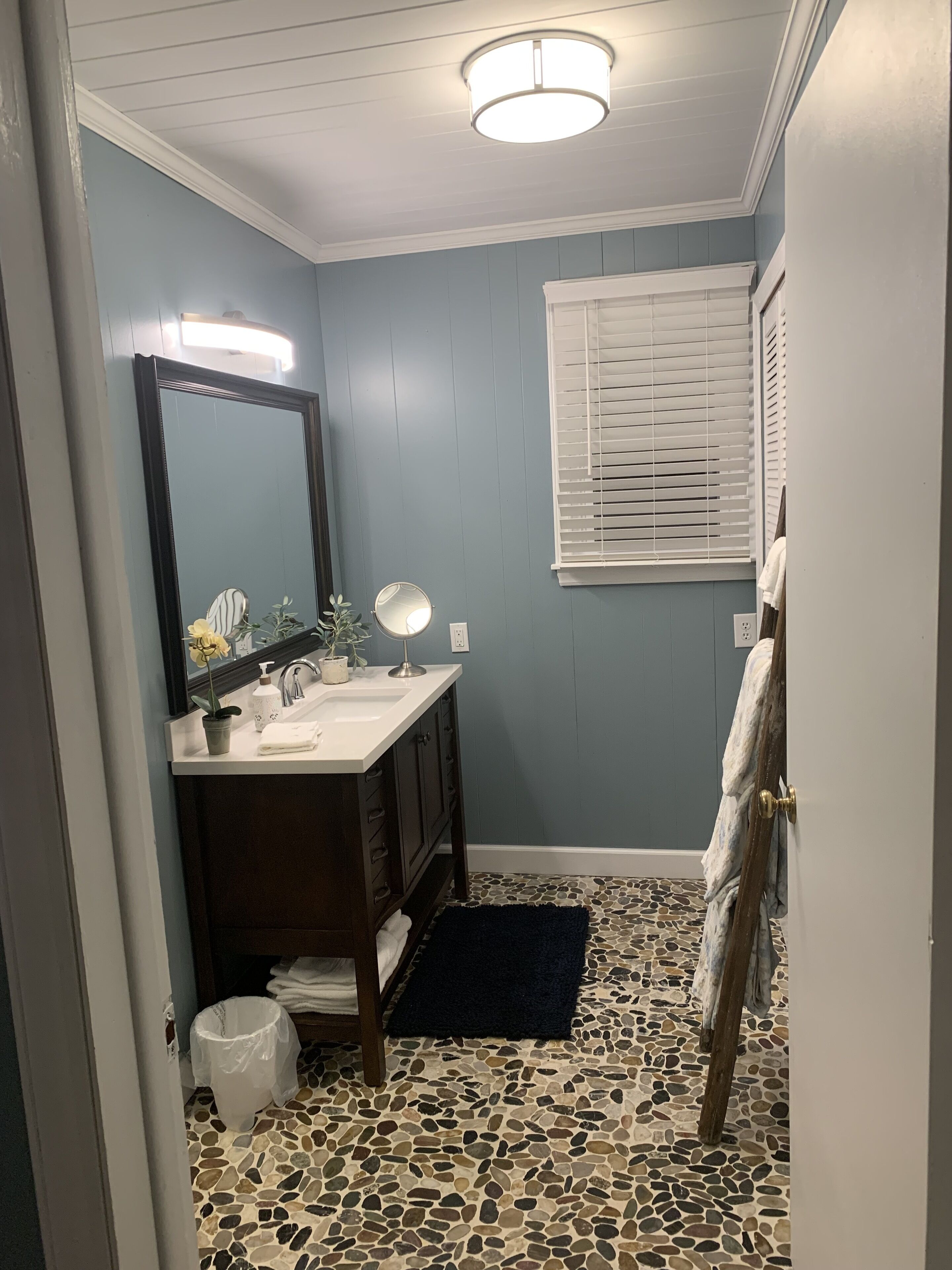 A bathroom with a sink, mirror, and window with blinds.