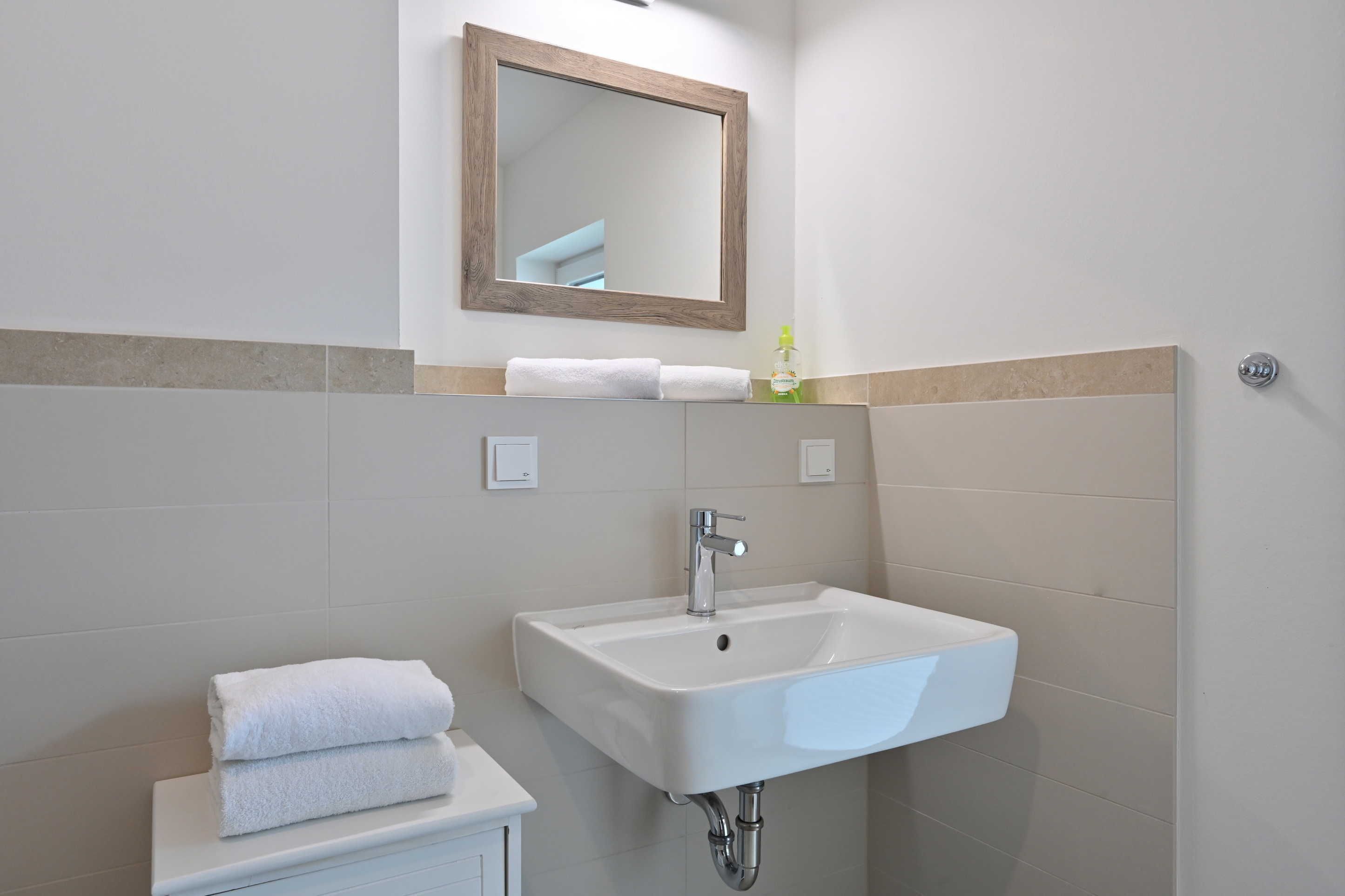 Un baño con un lavamanos blanco, un espejo y un perchero para toallas.