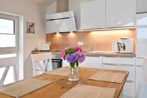 Une cuisine moderne avec des armoires blanches, un plan de travail en bois, une machine à café et un vase rempli de fleurs sur la table.