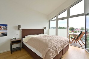 Een slaapkamer met een groot bed, een nachtkastje, een lamp en uitzicht op een balkon met buitenmeubilair.