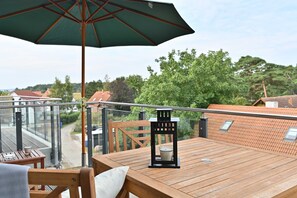 Een houten terras met een tafel, stoelen, een groene parasol en een lantaarn.