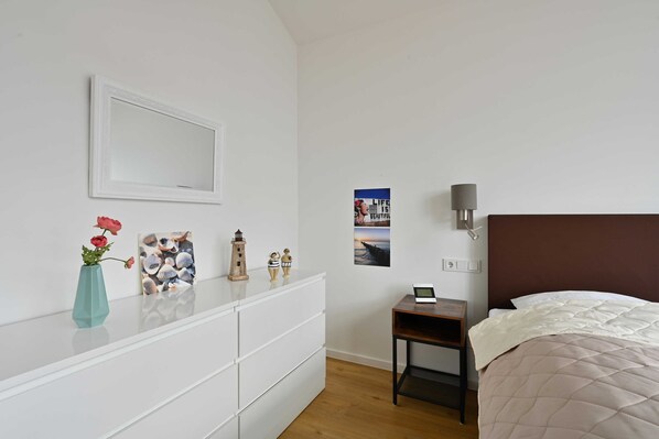 Une chambre à coucher comprenant un lit, une table de chevet avec une lampe, une commode, un miroir et des éléments de décoration murale, notamment une affiche.
