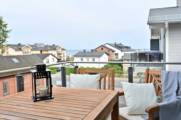 Een houten terras met een tafel, stoelen, een lantaarn en een uitzicht op huizen en water.