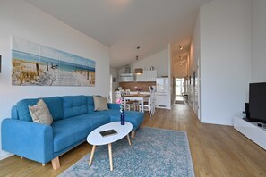 Un salon moderne avec un canapé bleu, une petite table blanche et un tableau sur le thème de la plage accroché au mur.