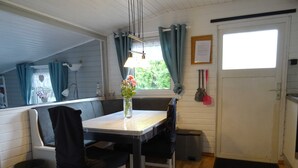 A cozy room with a wooden floor, a table with chairs, a bench, a window with curtains, a door, and a small trash bin. - Frehmeyer: Vacation on the farm - Ferienhaus Frehmeyer (Lindewitt)