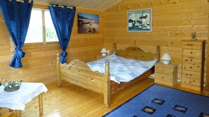 A wooden cabin bedroom with a bed, a nightstand, a dresser, and a table with a lace tablecloth. - Frehmeyer: Vacation on the farm - Ferienhaus Frehmeyer (Lindewitt)