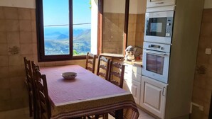 A dining area with a table set for two, a bowl of cereal, and a view of mountains through a large window. - Family home with sea view near St-Florent (Rutali)