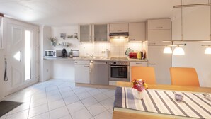 A modern kitchen with white cabinets, stainless steel appliances, and a dining area with a striped tablecloth. - Ihr Ruhepol im Naturschutzgebiet am Ihlsee! Wellness für die Seele! (Bad Segeberg)