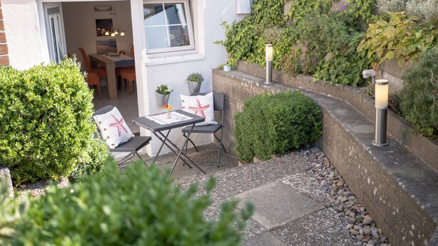 A patio with a table and chairs, surrounded by greenery and a stone wall. - Ihr Ruhepol im Naturschutzgebiet am Ihlsee! Wellness für die Seele! (Bad Segeberg)