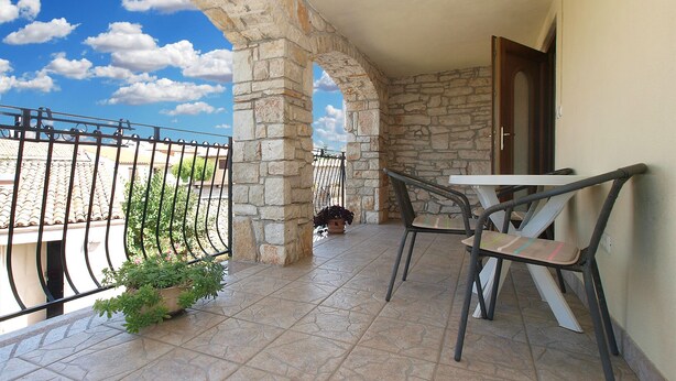 Un balcon orné d’arches en pierre, avec une table, des chaises et un pot de fleurs.