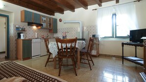Une cuisine avec des meubles de rangement en bois, une table à manger avec des chaises, un petit réfrigérateur et une fenêtre avec des rideaux.