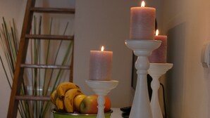 A table with three white candle holders, each with a lit candle. A green bowl with fruits is on the table. - Alojamiento Rural con Encanto La Casona del Piquero (Lastres)