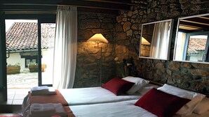 A hotel room with two beds, a stone wall, a dining area with a table and chairs, and a view of the outside. - Alojamiento Rural con Encanto La Casona del Piquero (Lastres)