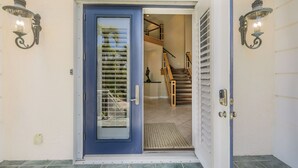 A blue door with a glass panel, a wooden staircase, and two wall-mounted light fixtures. - ROYAL PALM HOUSE - Luxury Style 3 Bedroom Home On Captiva With Private Pool (Captiva)