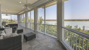A spacious balcony with wicker furniture, a ceiling fan, and a view of a lake. - ROYAL PALM HOUSE - Luxury Style 3 Bedroom Home On Captiva With Private Pool (Captiva)