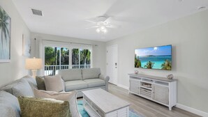 A living room with a sofa, coffee table, TV, and a view of the outdoors. - Seashells #39 |July & August Discounts! 3 Night Min. Stays! (Sanibel)