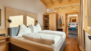 A bedroom with a wooden ceiling, a bed with white bedding, a wooden wardrobe, and a bathroom with a mirror and sink. - Chalet Häuser (oetz)