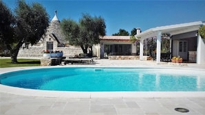 Une piscine avec un bâtiment en pierre en arrière-plan, un patio couvert et un chemin en pierre menant à la piscine.