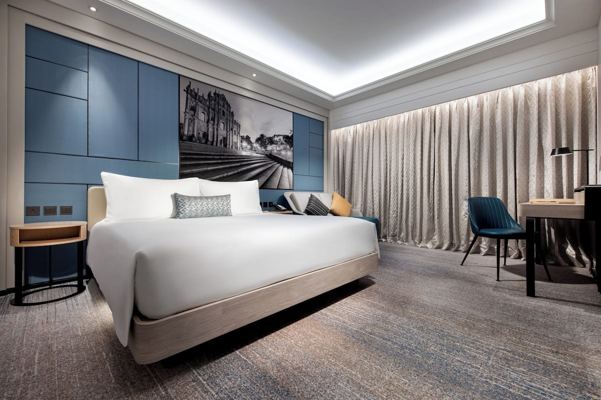 Habitación de hotel moderna con una cama grande, un escritorio, una silla y un ventanal con cortinas.