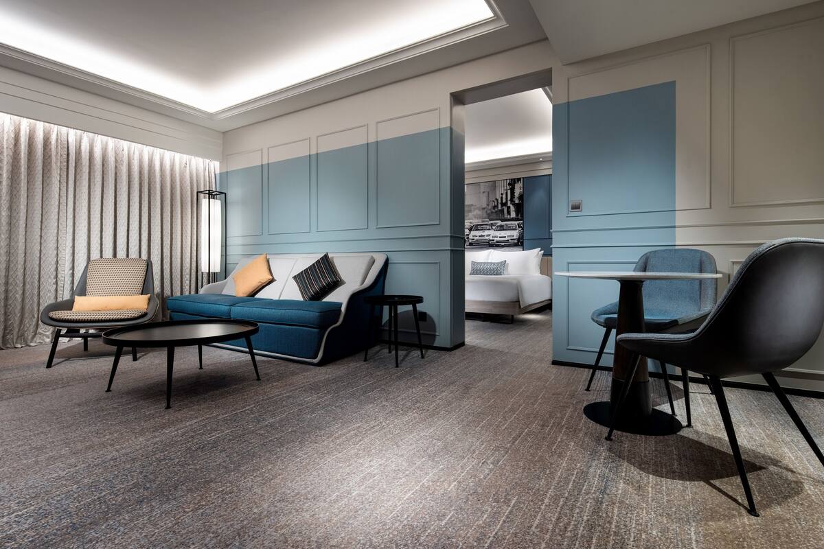 Una habitación de hotel moderna con una pared azul de acento, un sofá, una silla, una mesita y una cama.