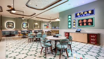 A modern hotel lobby with round tables, green chairs, and a patterned floor.