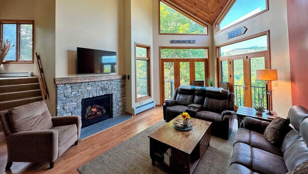 A spacious living room with a stone fireplace, leather sofas, and large windows offering a view of the outdoors.