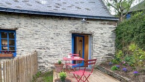 Een stenen gebouw met een houten terras, een rode tafel en stoelen, en een blauwe deur.