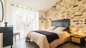 A bedroom with a stone wall, a bed with a headboard, a nightstand, a desk, and a chair. - "Charming Cottage with Private Garden, Jacuzzi, and Bikes – Near Nantes & Beach" (Port-Saint-Père)