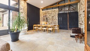 A spacious dining area with a stone wall, wooden beams, and a large window. - "Charming Cottage with Private Garden, Jacuzzi, and Bikes – Near Nantes & Beach" (Port-Saint-Père)